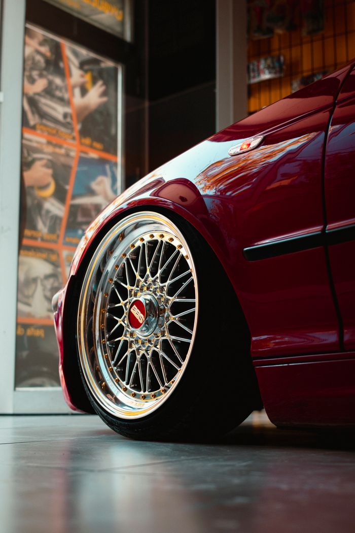 gallery-5 Detailed view of a custom red sports car wheel, showcasing intricate alloy design indoors.