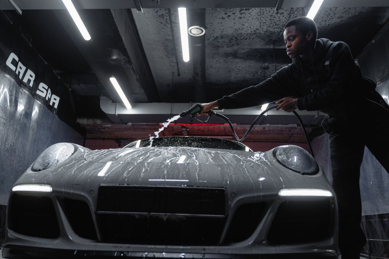 hero-img-01 African American man cleaning a white sports car at an indoor car wash. Low angle perspective.