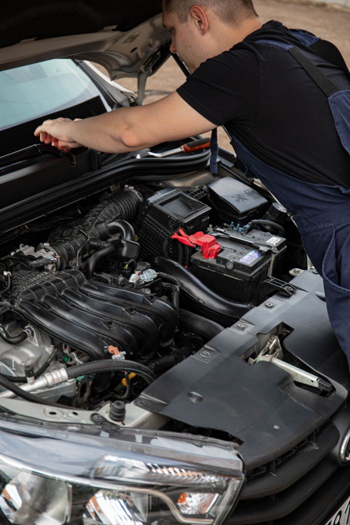 gallery-1 Mechanic in overalls fixing a car engine, focusing on maintenance and repair outdoors.